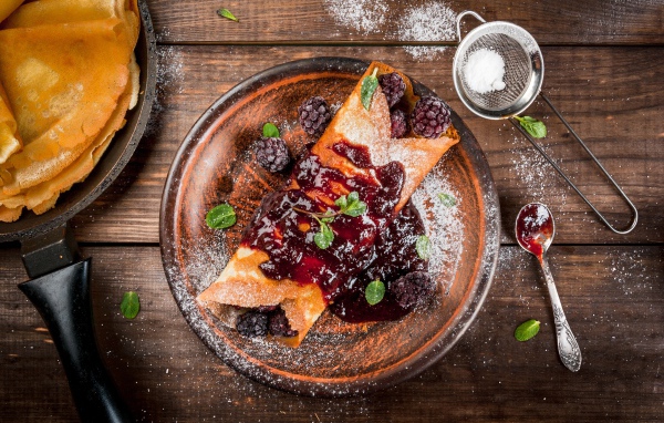 Блин с ягодами и джемом на тарелке с сахарной пудрой