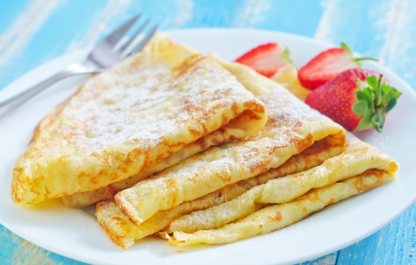 Румяные тонкие блинчики на тарелке с клубникой 