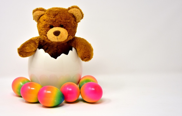 Медвежонок с яркими пасхальными яйцами на сером фоне