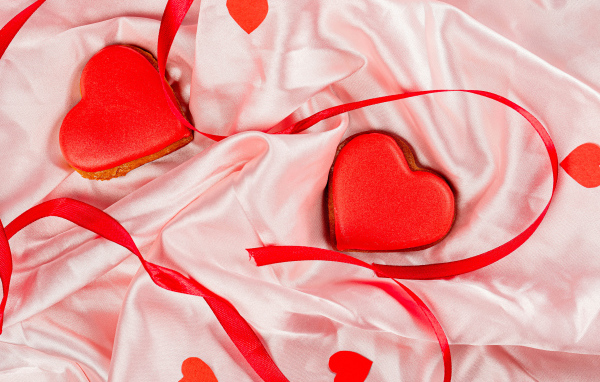 Два красных сердечка с ленточкой на розовой ткани на день влюбленных