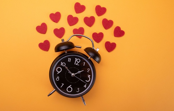 Черный будильник с сердечками на оранжевом фоне