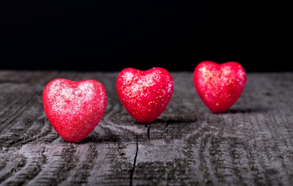 Блестящие красные сердечки на деревянном столе