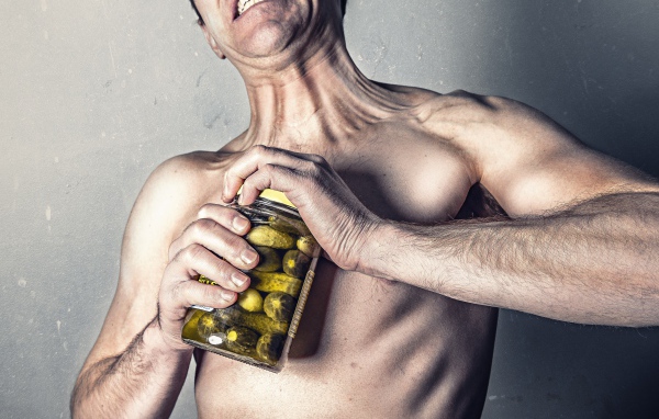 Мужчина открывает банку с огурцами на сером фоне 