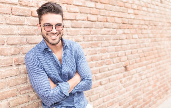 Улыбающийся мужчина в очках стоит у стены 