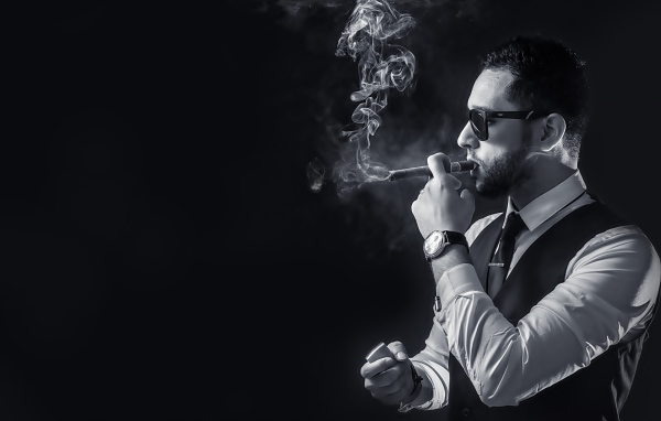 Мужчина с сигарой в руке на черном фоне 
