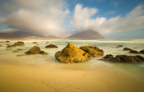 Большие камни лежат в воде на песке 