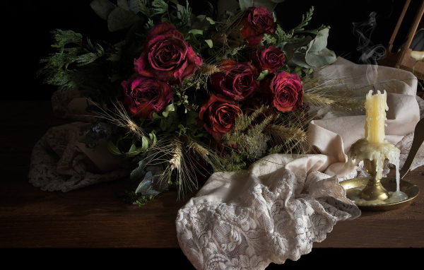 Завядший букет роз со свечой на столе