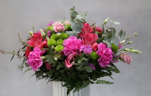 Красивый разноцветный букет в белой вазе на фоне серой стены 