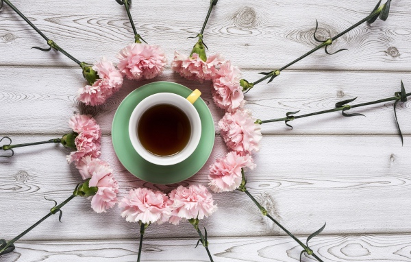 Розовые гвоздики с чашкой чая на деревянном столе 