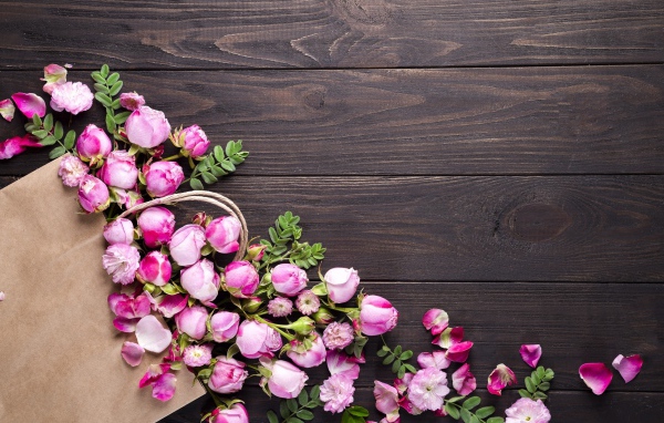Цветки розовой розы с бумажным пакетом  на деревянном фоне
