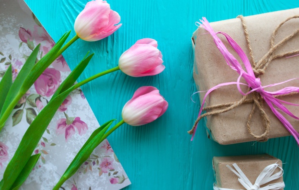 Три розовых тюльпана на голубом столе с подарками