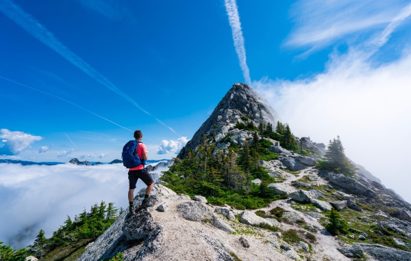 Мужчина подымается на вершина горы под голубым небом 