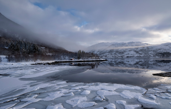 Покрытое льдом холодное озеро у гор в тумане