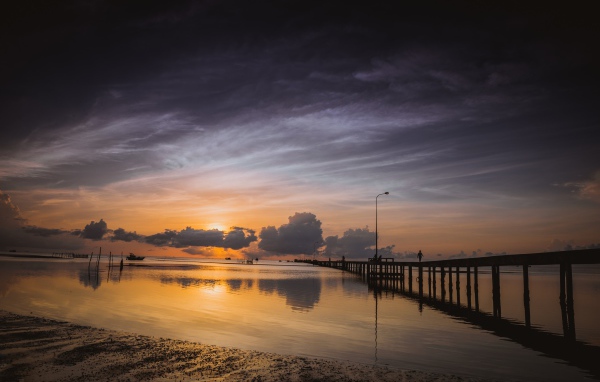 Деревянный мост на реке в лучах  солнца на закате