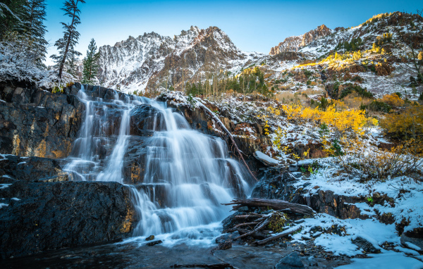 Красивый водопад стекает по холодным камням на фоне заснеженных гор