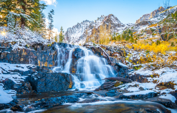 Водопад стекает по покрытым снегом камнях в горах