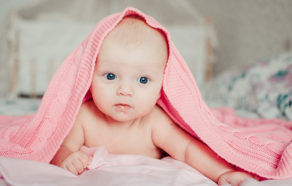 Грудной ребенок лежит под розовым пледом
