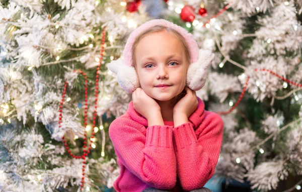 Девочка в розовых наушниках сидит у ели