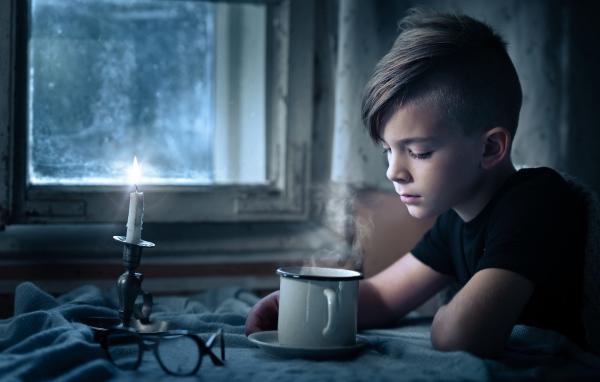 A little boy sitting at a table by the light of a candle