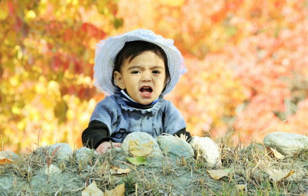 Маленькая девочка в шляпке сидит на земле