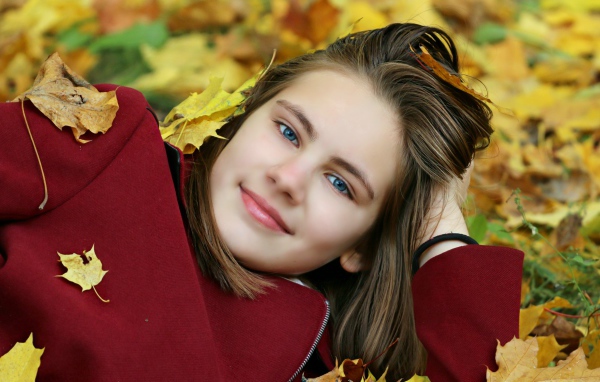 Красивая голубоглазая девочка лежит на опавшей листве