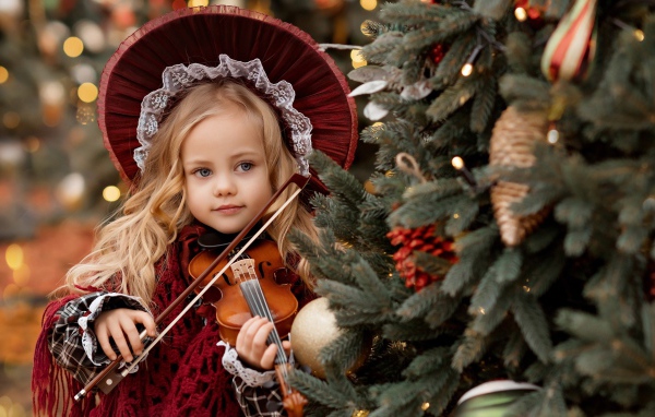 Красивая маленькая девочка со скрипкой у ели