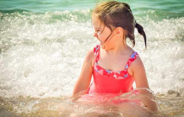 Веселая маленькая девочка в купальнике сидит в воде 