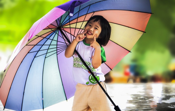 Маленькая девочка азиатка под большим разноцветным зонтом 