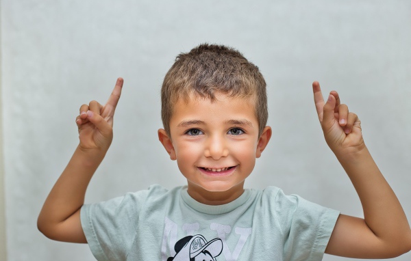 Маленький мальчик поднял руки вверх на сером фоне