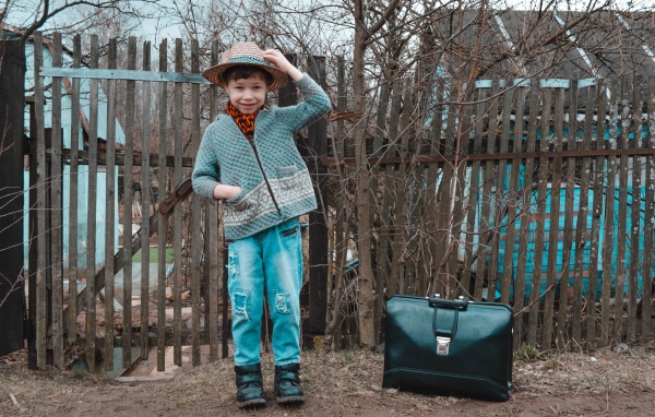 Маленький мальчик с чемоданом у забора