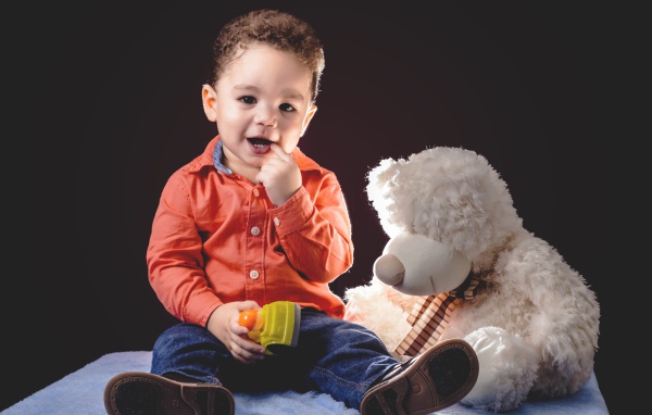 Маленький мальчик с игрушечным медведем на черном фоне