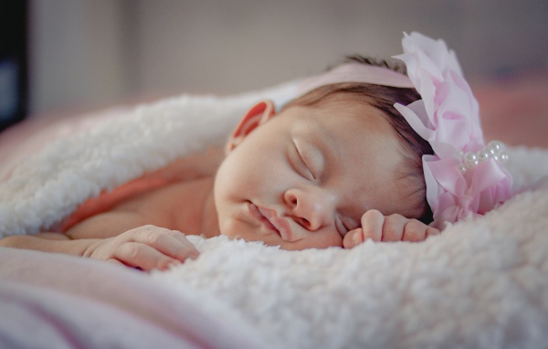 Маленькая грудная девочка с цветком на голове на кровати 