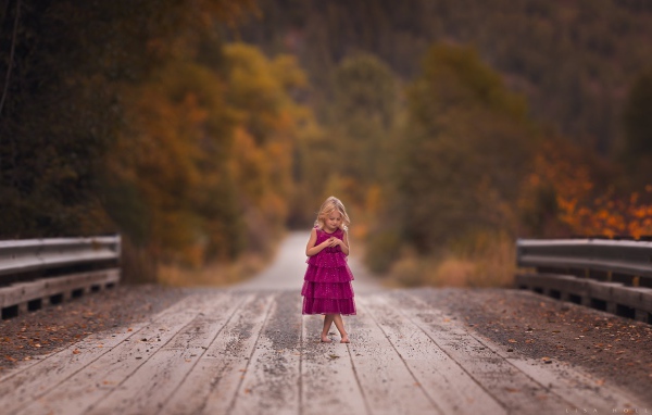 Маленькая девочка в платье стоит на мосту 