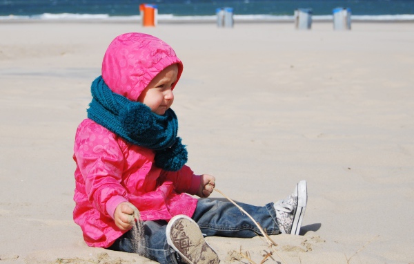 Маленькая девочка в розовой куртке на песке