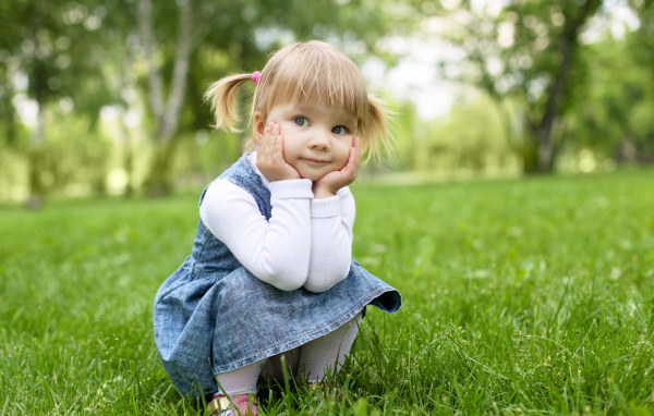 Маленькая девочка в сарафане сидит на траве 