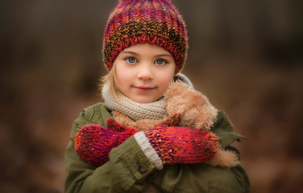 Маленькая девочка в теплой шапке и варежках  с игрушкой в руках 