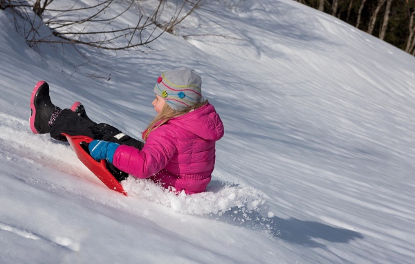 Маленькая девочка катится с заснеженной горки 