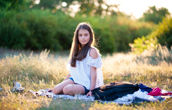 Маленькая девочка сидит на покрывале на земле 