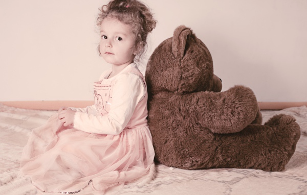 Маленькая девочка сидит с большим медведем