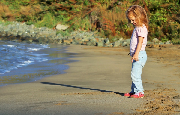 Маленькая девочка гуляет по мокрому песку 