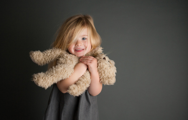 Маленькая девочка с игрушечным медвежонком в руках  на сером фоне 