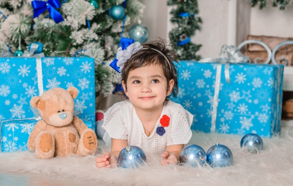 Маленькая девочка с подарками и игрушками под елкой 