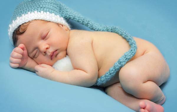 Маленький спящий ребенок в шапке на голубом фоне 