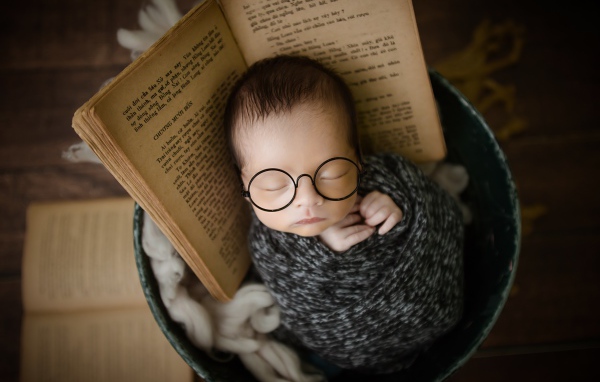 Маленький спящий ребенок в ведре с книгой 
