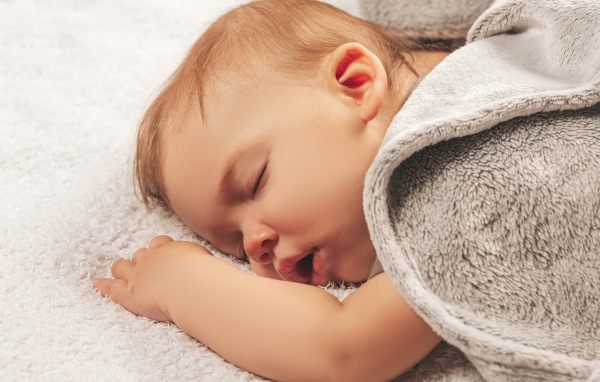 Маленький спящий ребенок под серым покрывалом 