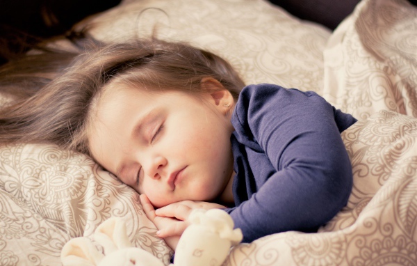 Маленькая спящая девочка на кровати с игрушкой 
