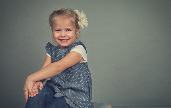 Маленькая улыбающаяся девочка с бантом на сером фоне 