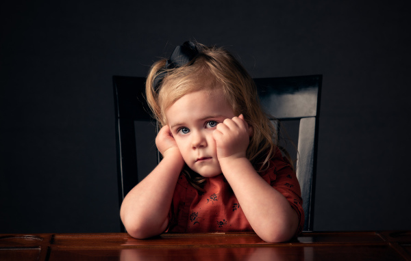 Грустная маленькая девочка сидит за столом