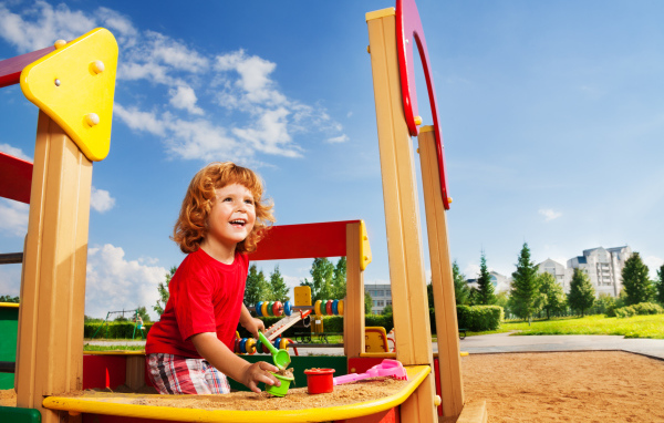 Улыбающийся мальчик в песочнице на детской площадке 