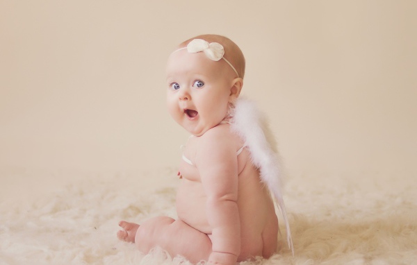 Удивленный грудной ребенок с белыми крыльями за спиной 